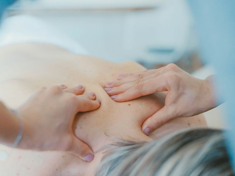 Hands working on the muscles around a patient's shoulder blade