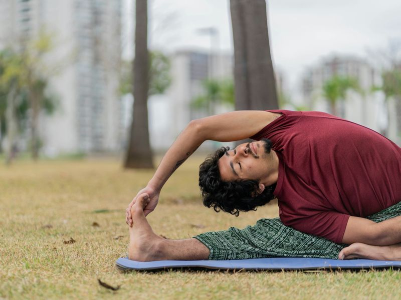 Man doing a seated side stretch on a mat outdoors